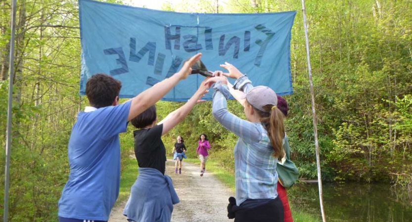 In the background, two students run forward toward a banner that appears to read "finish line." In font of the banner, four people make an archway with their lifted arms.